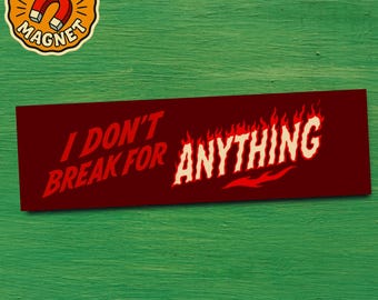 Op de afbeelding: Rode bumpersticker met de tekst "I DON'T BREAK FOR ANYTHING" in witte, vlamachtige letters. Een kleinere, cirkelvormige magneet met een magneetgrafiek staat in de linkerbovenhoek. De achtergrond is een getextureerd groen.