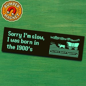 Könnte beinhalten: Ein schwarzer Stoßfängeraufkleber mit dem Text "Sorry I'm slow, I was born in the 1900's" in einer Retro-Pixel-Schriftart. Der Aufkleber zeigt auch ein pixeliges Bild eines Planwagens und den Text "You have died of dysentery."