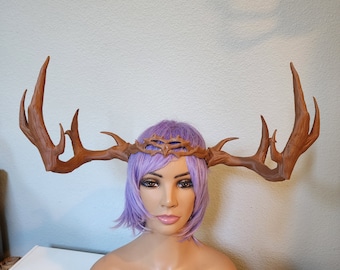 May include: A brown antler crown with a wire mesh design. The crown is worn on a mannequin with purple hair.