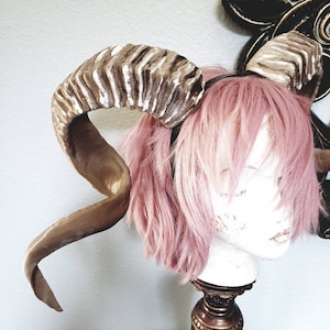 以下が含まれることがあります： 黒いヘッドバンドが付いた、茶色と白のフェイクラムホーンのペア。 ホーンはカールしていて、ベルベットのような質感です。