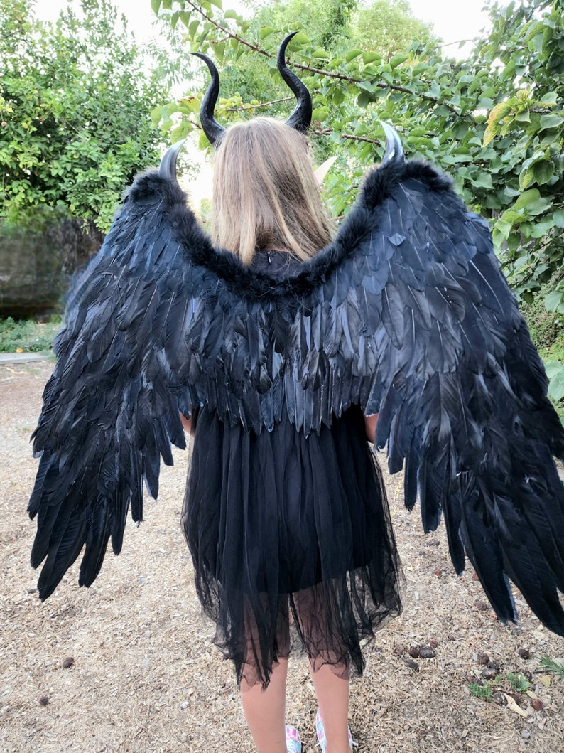 May include: Black feathered angel wings with a black tulle dress and black horns. The wings are large and dramatic, perfect for a costume or cosplay.