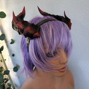 May include: A pair of red and black devil horns headband. The horns are made of a textured material and are attached to a black headband.