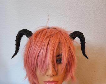 Könnte beinhalten: Ein schwarzes Stirnband mit zwei daran befestigten schwarzen Hörnern. Das Stirnband wird von einer Puppe mit pinkfarbenem Haar getragen.
