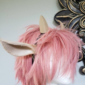 May include: A pair of light brown faux fur ears and horns, worn on a pink wig. The horns are pointed and the ears are floppy.