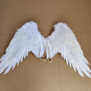 May include: White angel wings with a white ribbon tie. The wings are made of feathers and are designed for costume or cosplay.
