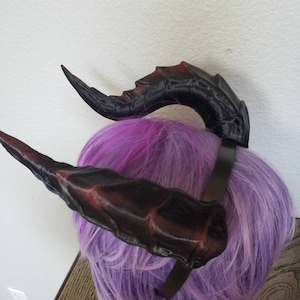 May include: A pair of black and red devil horns attached to a black headband. The horns are made of a soft, flexible material and have a textured surface.