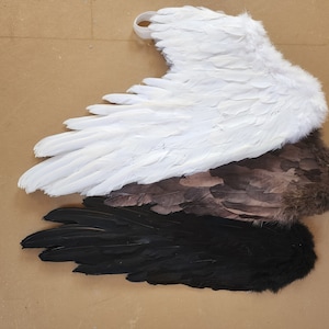 May include: Three pairs of angel wings in different colors: white, brown, and black. The wings are made of feathers and are arranged in a stack.