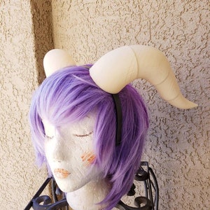 Puede incluir: Un par de accesorios para el cabello de diadema de cuerno blanco falso. Los cuernos son curvos y tienen una superficie texturizada. La diadema es negra.