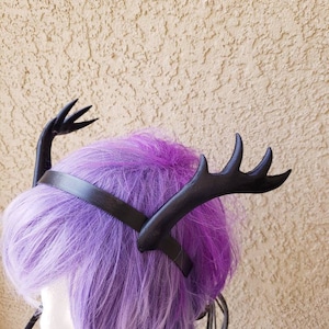 May include: Black faux leather deer antler headband with a wide band. The headband is worn on a purple wig.
