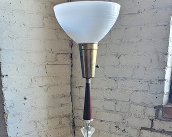 May include: A mid-century modern floor lamp with a white glass shade, a brass base, and a wooden accent. The lamp has a crystal-like detail in the middle of the pole.