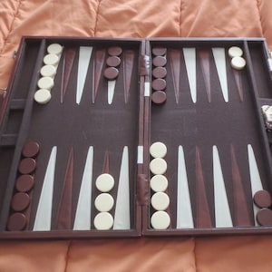 May include: A brown leather backgammon set with white and brown counters. The set is open and ready to play. The game board is made of felt and has a brown and white design. The set includes a small leather case for the dice.