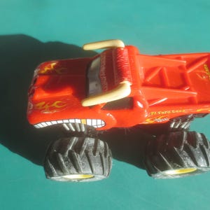 May include: A red toy monster truck with black tires and the text "El Toro Loco". The truck has a bull-like design with horns and a menacing grin. Flames are painted on the sides.