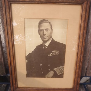 May include: Framed black and white portrait of a man in a dark suit with medals. The portrait is in a wooden frame with a light brown matting. The image is a vintage photograph.