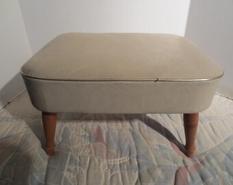 May include: A light beige upholstered footstool with wooden legs. The stool has a zippered top.