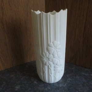 May include: White ceramic vase with a fluted design and embossed flower details.