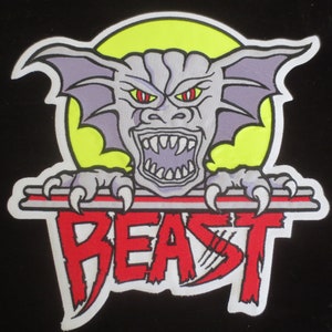 May include: A patch featuring a cartoonish, gray gargoyle with red eyes and sharp teeth, set against a yellow circle. The word "BEAST" is written in red, outlined in white, below the creature.