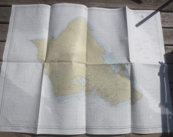 Può includere: Carta nautica piegata di un'isola, con contorni terrestri e marini beige e blu. La carta è aperta, mostrando linee e segni dettagliati su più pannelli, progettata per la navigazione. La carta ha un aspetto vintage.