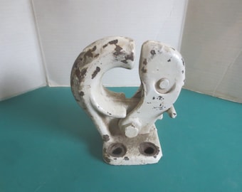 Può includere: Un gancio di traino in metallo resistente con una finitura verniciata di bianco che mostra segni significativi di usura e macchie di ruggine. Il gancio presenta un design curvo, un meccanismo di chiusura a cerniera e una piastra di base rettangolare.