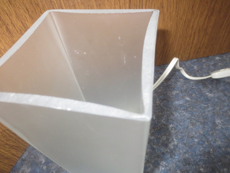 May include: A white frosted glass lampshade with a square base and a cord.