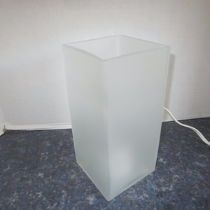 May include: A white frosted glass table lamp with a square base and a white cord.