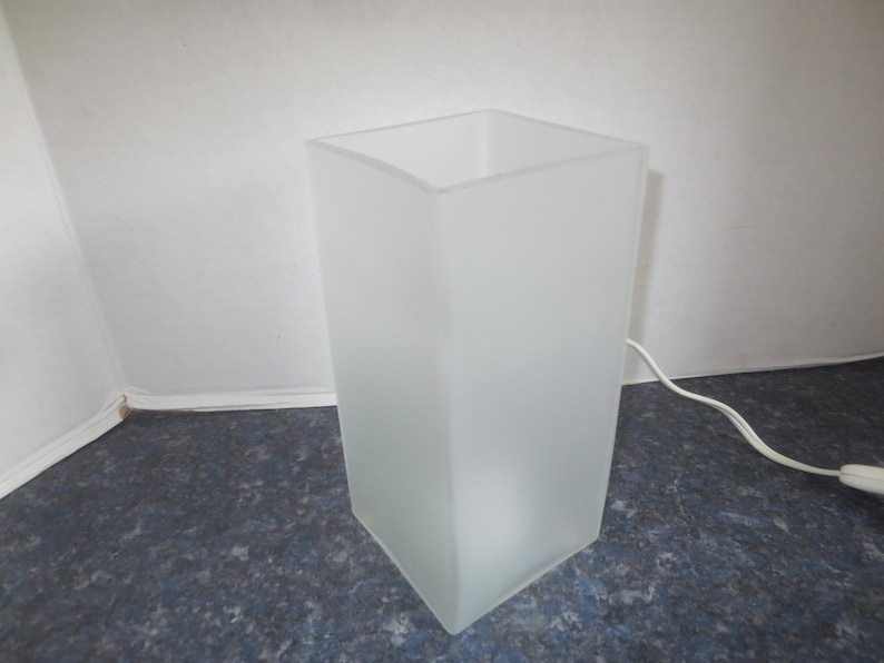 May include: A white frosted glass table lamp with a square base and a white cord.