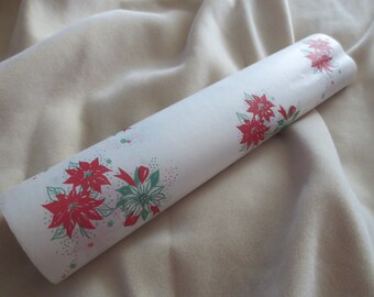 May include: A rolled white paper product decorated with red poinsettias and green accents. The floral design is repeated along the edge of the roll. The background is a soft, beige fabric.