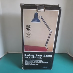 May include: A black and white box with a blue and white swing arm lamp. The box reads "Swing Arm Lamp with 2 section shade". The lamp has a 300 degree swivel flexible arm movement and extends to 32 inches. It takes up to a 100 watt bulb.