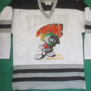 May include: White hockey jersey with black and grey stripes. The jersey features a cartoon image of Marvin the Martian with the text "Marvin! The Martian".
