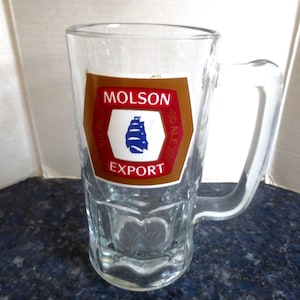 May include: A clear glass beer mug with a brown and red label that says "Molson Export Ale".