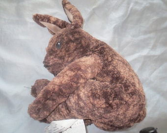 May include: A brown plush rabbit toy with a long, floppy ear. The rabbit is sitting on a white surface.