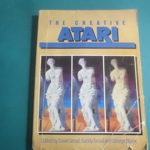 Peut inclure: Un livre vintage intitulé "The Creative Atari" avec une couverture beige. Le titre est en lettres bleues. La couverture présente trois images d'une statue blanche. Le livre est édité par David Small, Sandy Small et George Blank.