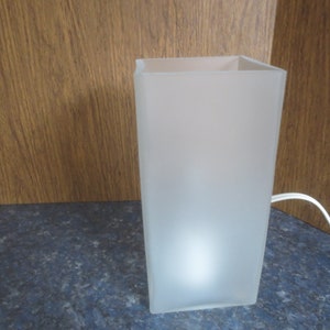 May include: A white frosted glass lamp with a square base and a white cord.