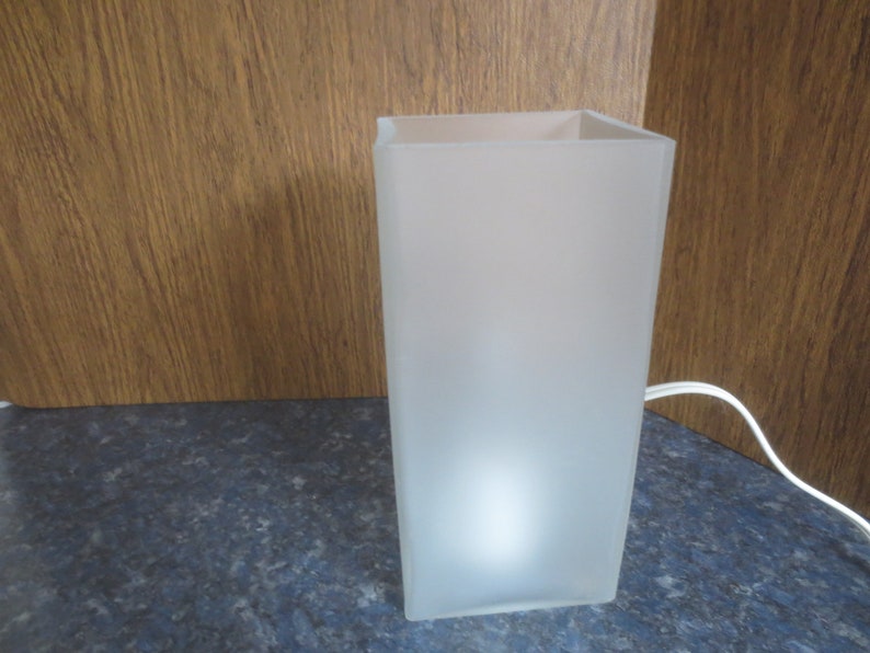 May include: A white frosted glass lamp with a square base and a white cord.