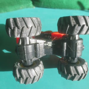 May include: A black and red toy monster truck with large, textured tires. The underside of the truck is visible, with the text "BOSS" and "&copy; 2001 MATTEL, INC. CHINA" printed on it. The tires are black with a textured tread.