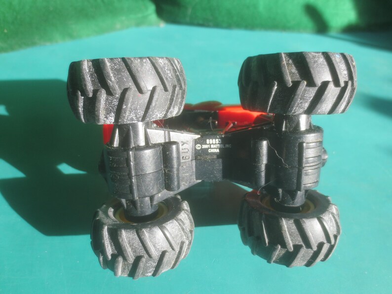 May include: A black and red toy monster truck with large, textured tires. The underside of the truck is visible, with the text "BOSS" and "&copy; 2001 MATTEL, INC. CHINA" printed on it. The tires are black with a textured tread.