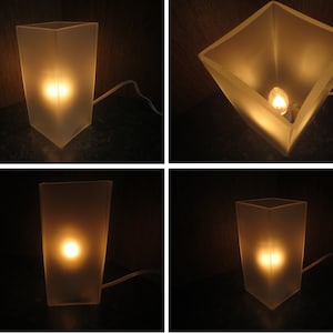 May include: A frosted glass table lamp with a light bulb turned on. The lamp is on a dark surface.