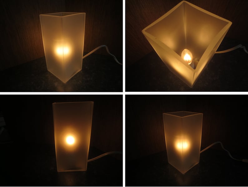 May include: A frosted glass table lamp with a light bulb turned on. The lamp is on a dark surface.