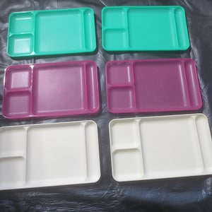 May include: Four plastic divided serving trays in green, pink, and white. The trays have three sections and a long handle.