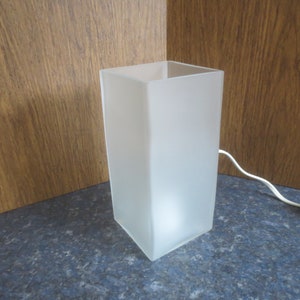 May include: A white frosted glass table lamp with a cord and plug.
