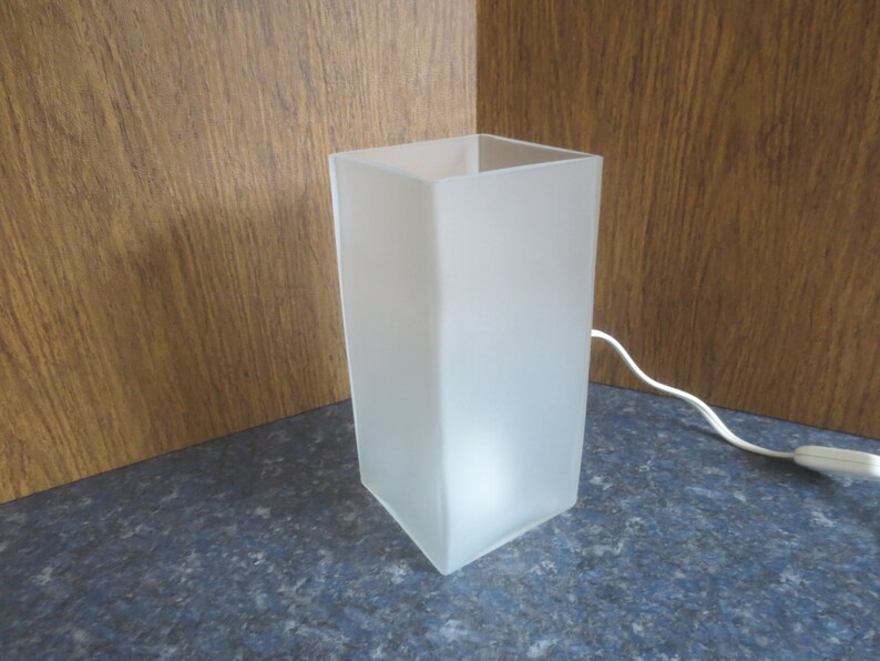 May include: A white frosted glass table lamp with a cord and plug.