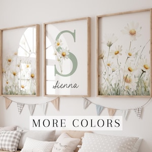 May include: Three framed prints with watercolor illustrations of white daisies on a white background. The middle print features the letter "S" in a light green color with the name "sienna" written below it.