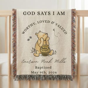 May include: A beige woven baby blanket with a Winnie the Pooh illustration and the text "GOD SAYS I AM WORTHY, LOVED & VALUED." The blanket also includes the name "Emerson Noah Mills," the word "Baptized," and the date "May 9th, 2026."