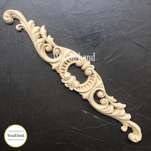 May include: A decorative wooden trim with a detailed, ornate design. The trim features a central oval shape with intricate scrollwork and a repeating pattern of lines. The trim is made of light-coloured wood and is suitable for adding a touch of elegance to furniture or home decor projects.