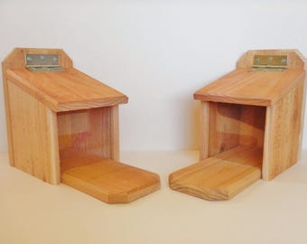 May include: Two wooden bird feeders with hinged doors. The feeders are made of natural wood and have a simple design.