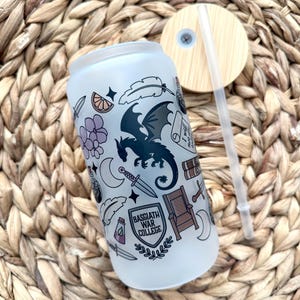 May include: A white frosted tumbler with a black dragon and other illustrations. The tumbler has a black and white shield with the text "Basgiath War College".