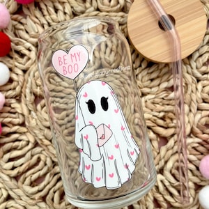 Peut inclure: Un gobelet en verre transparent avec un fantôme tenant un ballon en forme de cœur qui dit "Be My Boo". Le fantôme porte un motif de cœurs roses. Le gobelet a un couvercle en bambou et une paille transparente.