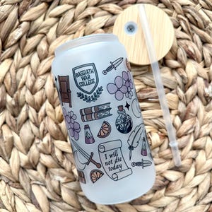 May include: A white frosted glass water bottle with a straw and a wooden lid. The bottle has a design of various illustrations including a shield with the text "Basgiath War College", a sword, a book, a potion bottle, a feather, a bunch of grapes, an orange slice, and a scroll with the text "I will not die today".