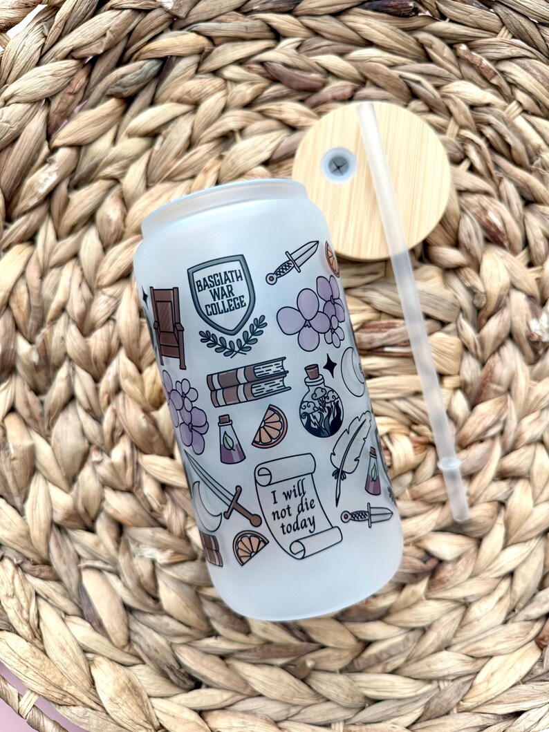 May include: A white frosted glass water bottle with a straw and a wooden lid. The bottle has a design of various illustrations including a shield with the text "Basgiath War College", a sword, a book, a potion bottle, a feather, a bunch of grapes, an orange slice, and a scroll with the text "I will not die today".