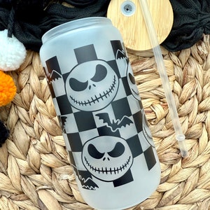May include: A frosted glass tumbler with a black and white checkered pattern and a repeated image of Jack Skellington from the Nightmare Before Christmas. The tumbler has a bamboo lid with a hole for a straw.