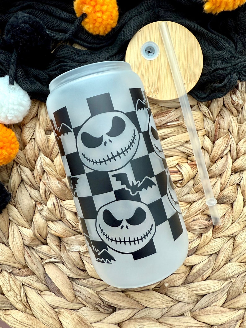 May include: A frosted glass tumbler with a black and white checkered pattern and a repeated image of Jack Skellington from the Nightmare Before Christmas. The tumbler has a bamboo lid with a hole for a straw.